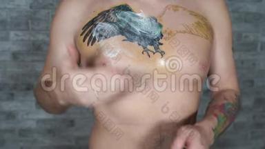 男人在胸前不完整的纹身上涂抹奶油。 男人的特写`用手把药膏涂抹在身体的一部分。